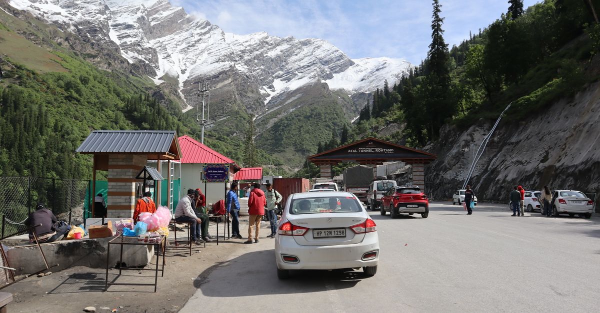 Bustling scene near Atal Tunnel with mountains, snow, and local vendors.